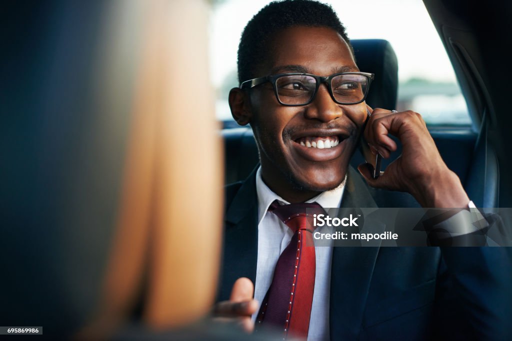 Shot of a happy young businessman making a call on his smartphone while traveling in the back seat of a car